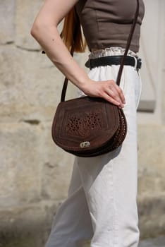 small brown women's leather bag with a carved pattern. street photo