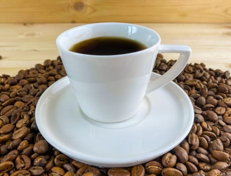 Coffee in a cup, coffee grains. Coffee in a cup with a saucer, coffee grains on a wooden table.