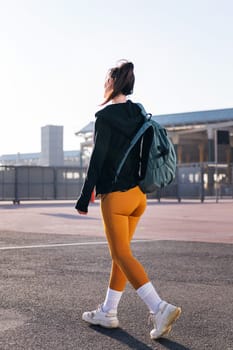 vertical photo with rear view of a sports woman walking along the street, concept of active lifestyle and urban sport