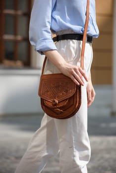 small brown women's leather bag with a carved pattern. street photo