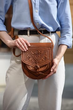 small brown women's leather bag with a carved pattern. street photo