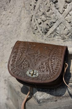 small brown women's leather bag with a carved pattern. street photo