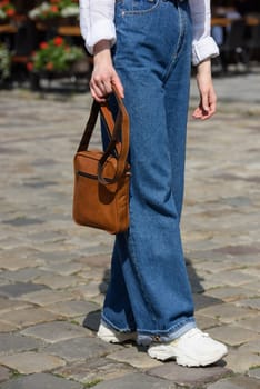 photo of a woman with a small yellow leather bag. the girl is dressed in jeans, a white blouse and sneakers