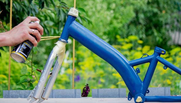 the father paints the child's bicycle with blue paint. selective focus