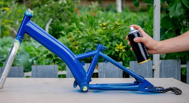 the father paints the child's bicycle with blue paint. selective focus