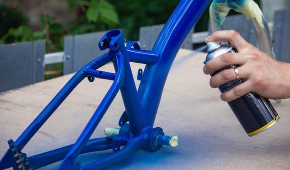 the father paints the child's bicycle with blue paint. selective focus