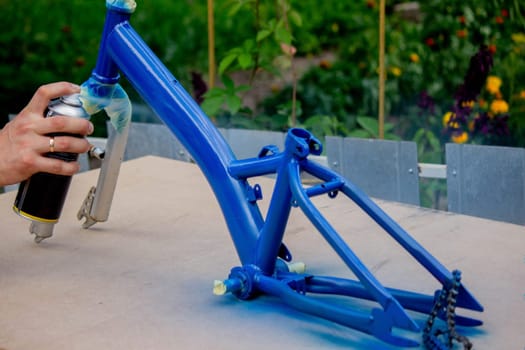 the father paints the child's bicycle with blue paint. selective focus