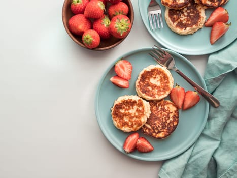 Sweet cheese pancakes on plate served strawberries. Cottage cheese pancakes, syrniki, ricotta fritters, curd fritters. Top view or flat lay. Copy space for text or design.