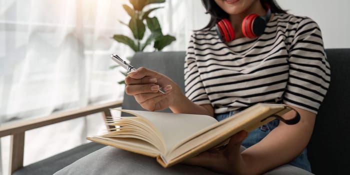 Close up view of woman sit at sofa hold pencil take notes to paper notebook working studying. Female student businesswoman employee write records to daily planner by hand at home work desk.