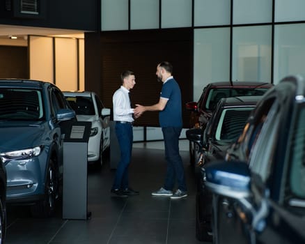 Seller and buyer shake hands in a car dealership. Caucasian man buys a car