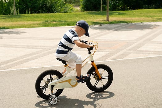 Sport concept. Boy on a bike. A small beautiful, happy, Caucasian boy 4 years old in a cap and a striped T-shirt rides a bicycle along the bike path in the summer outdoors.