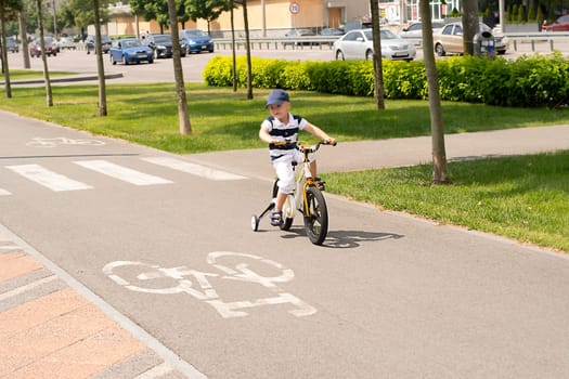 Sport concept. Boy on a bike. A small beautiful, happy, Caucasian boy 4 years old in a cap and a striped T-shirt rides a bicycle along the bike path in the summer outdoors.