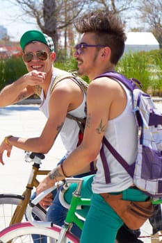 Men, students and friends with back, bicycle and sustainable transportation on road in summer sunshine. Young gen z people, retro bike and outdoor together in street with travel on university campus.