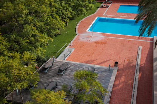 A sunny day at a hotel's outdoor relaxation area with a swimming pool, sunbeds, and an outdoor shower amidst lush greenery, providing a tranquil and relaxing setting.