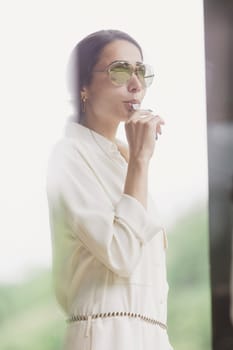 Portrait of attractive brunette holding whistle in her hand. Fashionable young woman with long hair in white costume standing in interior. Fan, coach, counselor