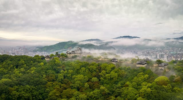 Aerial view of early morning fog over Matsuyama Castle on hill by city. High quality photo