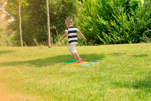 A child cheerfully runs barefoot on massage, multi-colored orthopedic rugs in the fresh air, in a green park in summer. Health concept. copy space.