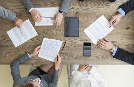 Business team working with contract, financial reports and laptop dicussing deal sitting around office table