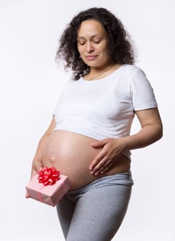 Happy Mother's and International Women's Day. Pregnancy. Maternity. Procreation. Childbirth. Pregnant woman, expectant gravid female with naked belly, holding a gift box over white isolated background
