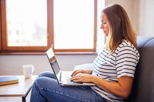 Young woman with a laptop and a cup of coffee on the table at home. Woman looking at laptop screen, reading good news in message, watching video, chatting in social network or shopping online.