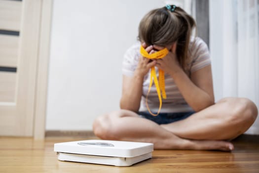 White scale and depression, upset and sad woman with measuring tape on wooden floor.