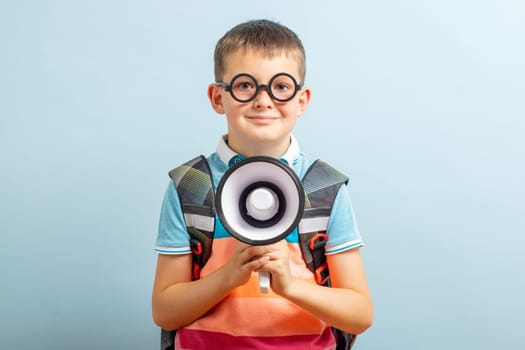 Little schoolboy with megaphone on blue background. Boy with megaphone making an announcement with copy space.