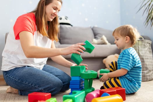 Happy loving family plays with plastic blocks and have fun. Mother and her baby son play together.