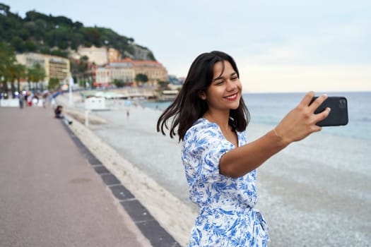 Beautiful smiling young woman takes selfie with a smartphone at the Promenade des Anglais in Nice, France