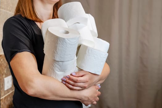 A woman holds many rolls of toilet paper. Consumer buying panic during Coronavirus outbreak . Crisis product lack concept.