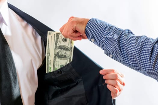Businessman in a suit takes dollar bills in his pocket as a bribe. Two person sealing the deal with bribe money. Corruption and bribery concept.