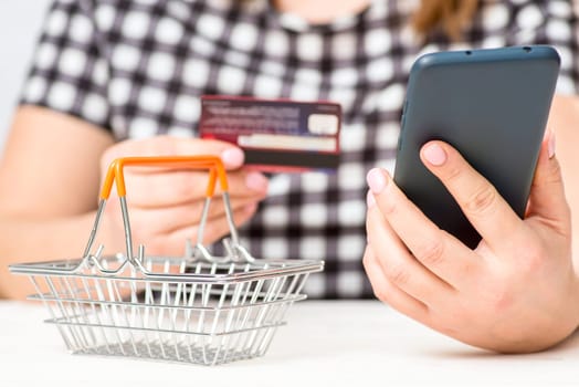 A woman holding plastic credit card and phone, making secure internet payment. A female customer shopping online.