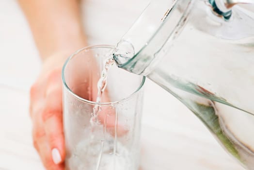A female is pouring fresh, clear water from a jug into a glass. Health and diet concept. Clean water for good health.