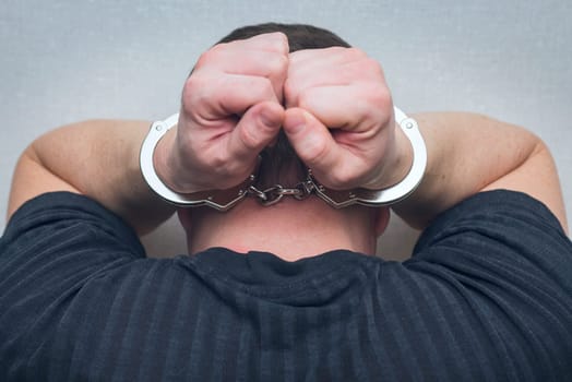 Criminal in handcuffs. Arrested man with hands in handcuffs behind his head.