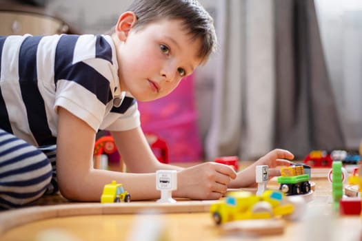 Cute boy is playing with toy railway road at home or in kindergarten on the floor. Child at home or in kindergarten.