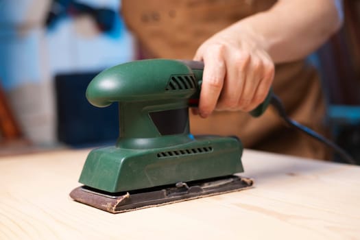 Closeup of carpenter sanding wooden planks with electrical sanding machine. A carpenter grinds wood with sander machine.