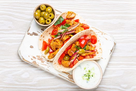 Traditional Greek Dish Gyros: Pita bread Wraps with vegetables, meat, herbs, olives on rustic wooden cutting board with Tzatziki sauce, olive oil top view, white wooden summer background.