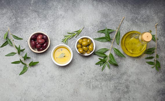 Composition with green and brown olives, extra virgin olive oil in glass bottle, olive tree branches on gray concrete stone rustic background overhead, Mediterranean concept