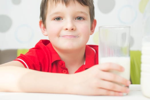 Little cute boy in a red t-shirt with a glass of milk in his hand. Child drinking milk.