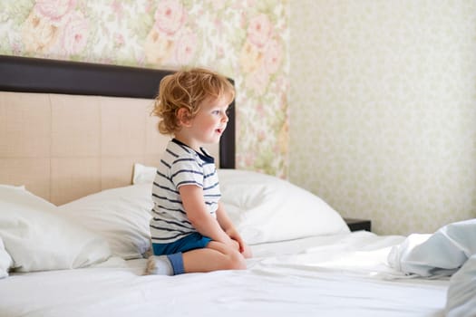 Cute laughing child boy sits in bed. Boy plays at home. Child in a sunny bedroom.