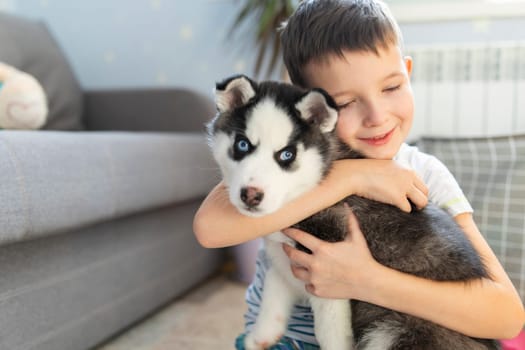 A boy sitting on the floor with his husky puppy. Child hugging his pup. Animal care. Birthday Surprise