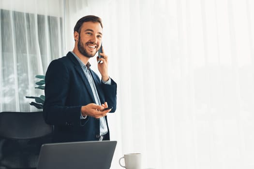 Hardworking businessman stand confidently in modern office making persuasive sales call to client. Office worker talking on the phone coordinate and manage business work with colleagues. Entity