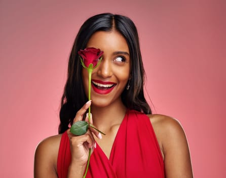 Excited, beauty and face of a woman with a rose on a studio background for valentines day. Makeup, model and happy young Indian girl with a flower in hand for romance or love on pink backdrop.
