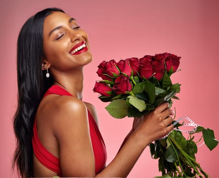 Happy, beauty and face of a woman with a roses on a studio background for valentines day. Makeup, model and young Indian girl with a flower bouquet and laugh for romance or love on a pink backdrop.