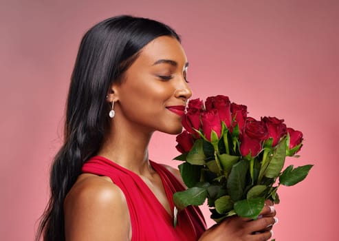 Face, beauty and a woman smelling a roses on a studio background for valentines day. Makeup, model and happy young Indian girl profile with a flower bouquet for romance or love on pink backdrop.