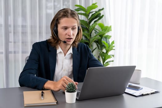 Male customer service operator or telesales agent sitting at desk in office, wearing headset and engage in conversation with client to provide support or close sales. Call center portrait. Entity