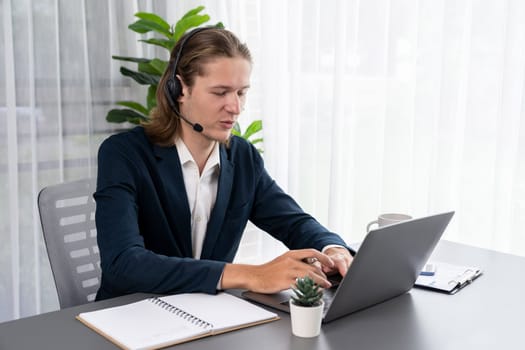 Male customer service operator or telesales agent sitting at desk in office, wearing headset and engage in conversation with client to provide support or close sales. Call center portrait. Entity