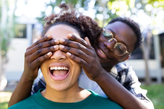 Young African American man covering eyes of surprised girlfriend. Focus on girl face. Loving relationship.