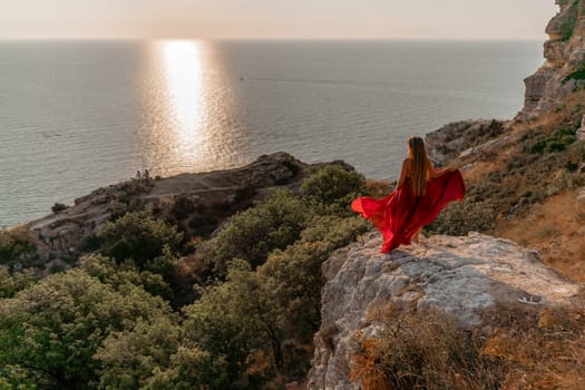 Woman sunset sea red dress, back view a happy beautiful sensual woman in a red long dress posing on a rock high above the sea on sunset