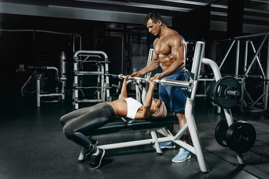 Fitness instructor exercising with his client at the gym. The beautiful blonde is engaged in sports. Handsome man, sports instructor