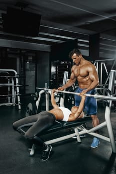 Fitness instructor exercising with his client at the gym. The beautiful blonde is engaged in sports. Handsome man, sports instructor